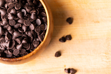 Overhead view of chocolate chips in bowl on wooden cutting board