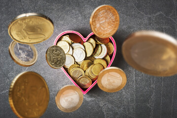 Euro currency coins falling in heart shaped box on grey stone background. Love and money concept