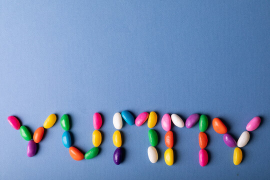 Directly above view of colorful candies arranged as yummy word on blue background with copy space