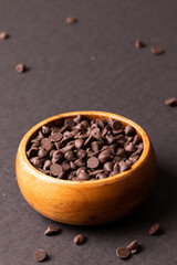 High angle view of fresh chocolate chips in wooden bowl against colored background
