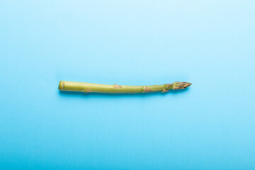 Fototapeta premium Directly above view of single raw green asparagus vegetable by copy space over blue background