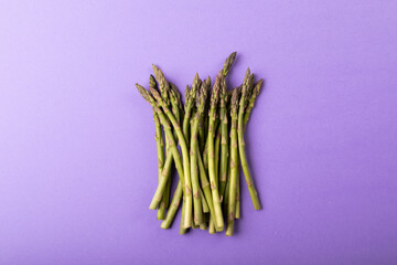 Overhead view of raw green asparagus vegetables by copy space against purple background - Powered by Adobe