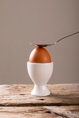 Close-up of spoon on fresh boiled brown egg in cup on table against gray background with copy space