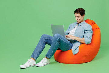 Full size body length young brunet man 20s wears blue shirt sit in bag chair hold use work on...