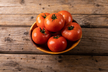 High angle view of fresh red tomatoes with water drops in bowl on wooden table