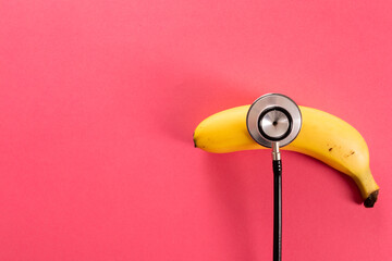 Overhead view of fresh banana with stethoscope by copy space over pink background - Powered by Adobe