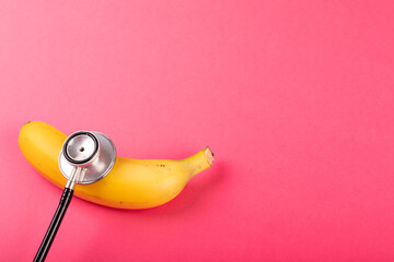 Directly above view of fresh banana with stethoscope by copy space on pink background