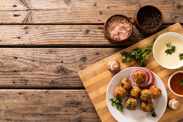 Directly above view of fresh meatballs with seasoning bowls on cutting board over wooden table