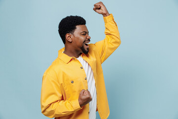 Side view young fun man of African American ethnicity in yellow shirt doing winner gesture...