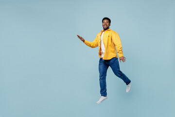 Full body side view young man of African American ethnicity 20s wear yellow shirt jump high walking going run isolated on plain pastel light blue background studio portrait. People lifestyle concept.
