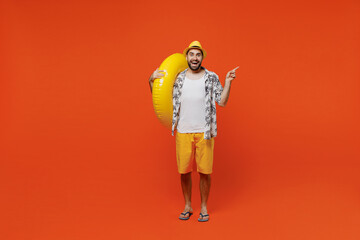 Full body young tourist man in beach shirt hat hold inflatable ring point index finger aside on...