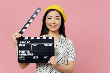 Young smiling woman of Asian ethnicity 20s wear white polka dot t-shirt yellow beret holding classic black film making clapperboard isolated on plain pastel pink background. People lifestyle concept. - obrazy, fototapety, plakaty