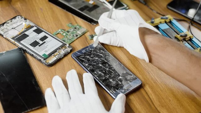 Shoulder shot of professional repairman removing broken display screen protector of mobile phone at shop - concept of expertise, skilled labour and safety
