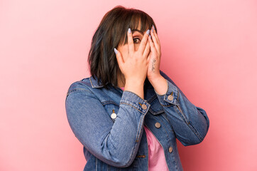 Young caucasian woman isolated on pink background blink through fingers frightened and nervous.