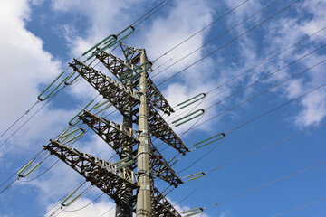 Power line support against the cloudy blue sky. High-voltage electricity transmission line