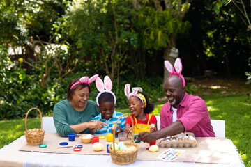 Fototapeta premium Cheerful african american siblings and grandparents in bunny ears painting eggs on easter day