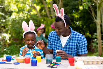 Fototapeta premium African american boy and father painting easter eggs while family in background