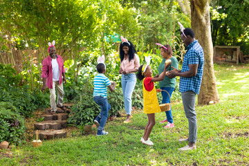 Naklejka premium African american multi-generational family in bunny ears with easter eggs in backyard