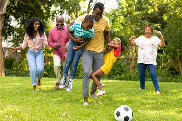 Foto op Canvas Playful african american multi-generational family playing soccer together in backyard on weekend © wavebreak3
