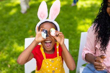 Cheerful african american girl and mother playing with easter eggs while family in background