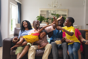 Happy african american multi-generational family high-fiving while watching rugby match on tv