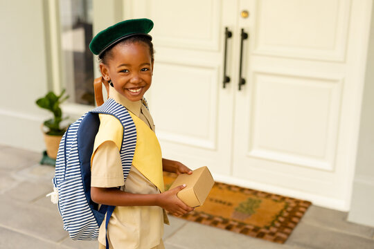 Smiling african american scout girl in uniform delivering package at home