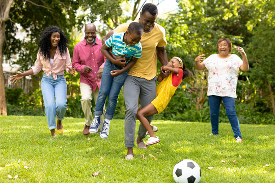 Playful african american multi-generational family playing soccer together in backyard on weekend