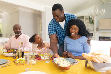 Smiling african american mid adult man serving food to family at dining table on thanksgiving day