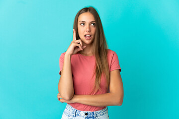 Young woman over isolated blue background thinking an idea pointing the finger up