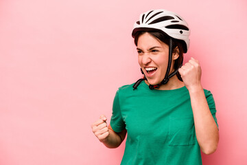 Young caucasian woman wearing helmet isolated on pink background raising fist after a victory, winner concept.