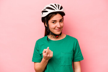 Young caucasian woman wearing helmet isolated on pink background pointing with finger at you as if inviting come closer.