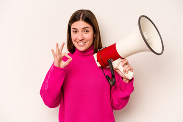Naklejka premium Young caucasian woman holding a megaphone isolated on white background cheerful and confident showing ok gesture.