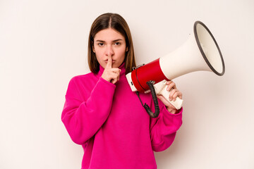 Young caucasian woman holding a megaphone isolated on white background keeping a secret or asking for silence.