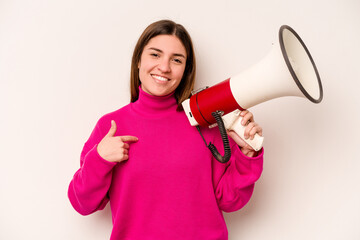 Young caucasian woman holding a megaphone isolated on white background person pointing by hand to a shirt copy space, proud and confident