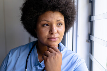 Close-up african american mid adult female nurse with hand on chin looking through window