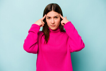 Young caucasian woman isolated on blue background focused on a task, keeping forefingers pointing head.