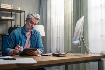 Mature man architect working on computer at desk indoors in office.