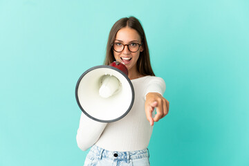Young woman over isolated blue background shouting through a megaphone to announce something while...