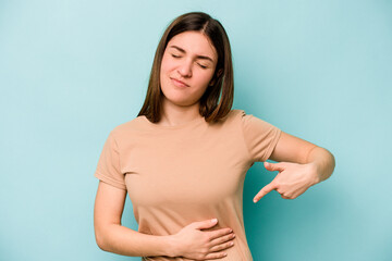 Young caucasian woman isolated on blue background having a liver pain, stomach ache.