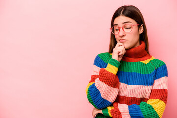 Young caucasian woman isolated on pink background looking sideways with doubtful and skeptical expression.