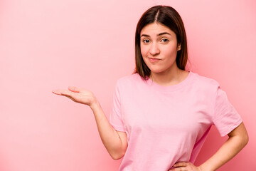 Young caucasian woman isolated on pink background showing a copy space on a palm and holding...