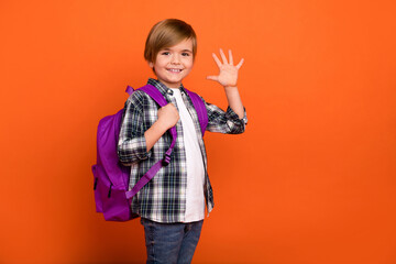 Profile side photo of young little boy waving hello meet friends isolated over orange color...