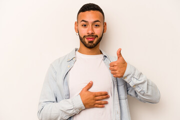 Young hispanic man isolated on white background touches tummy, smiles gently, eating and satisfaction concept.