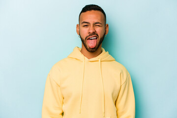 Obraz premium Young hispanic man isolated on blue background funny and friendly sticking out tongue.