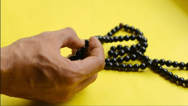 Close-up of a man reading a prayer with beads or an Islamic religious icon on a yellow background