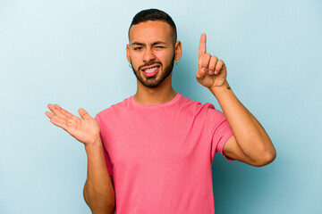 Fototapeta premium Young hispanic man isolated on blue background holding and showing a product on hand.