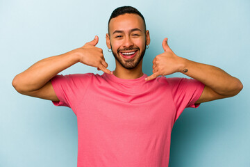 Young hispanic man isolated on blue background showing a mobile phone call gesture with fingers.