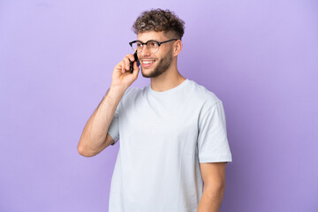 Delivery caucasian man isolated on purple background keeping a conversation with the mobile phone