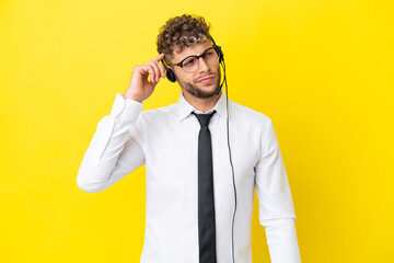 Telemarketer blonde man working with a headset isolated on yellow background having doubts and with confuse face expression