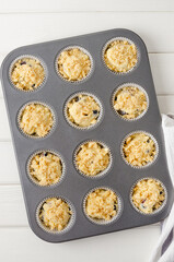Raw dough for lemon muffins with blueberries and shtreisel in baking form on a white wooden background. Recipe step by step. Top view.